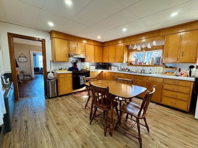 kitchen featuring light wood-type flooring, sink, a drop ceiling, and black appliances