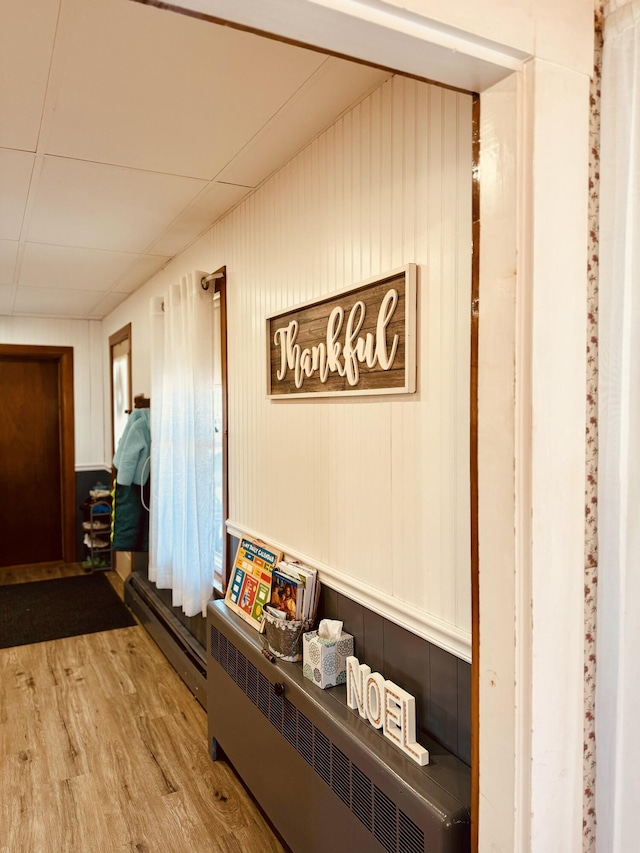 hall with wood-type flooring, wooden walls, and a baseboard radiator