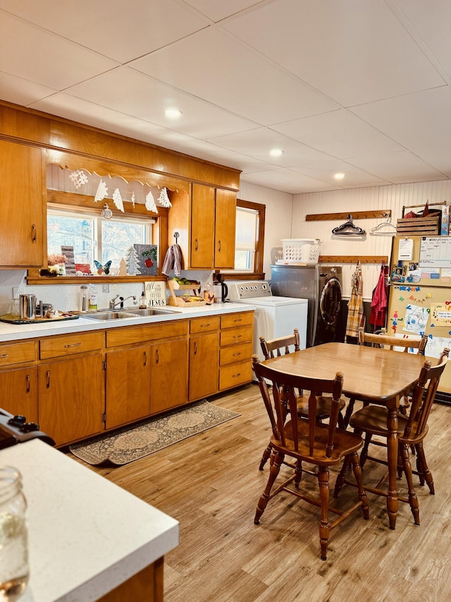 kitchen featuring sink, light hardwood / wood-style flooring, wood walls, and independent washer and dryer