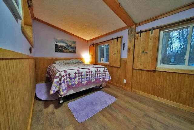 bedroom with a wainscoted wall, lofted ceiling with beams, a barn door, wooden walls, and wood finished floors