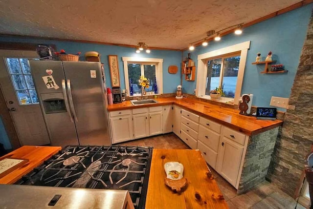 kitchen with a textured ceiling, a sink, wood counters, range with gas stovetop, and stainless steel fridge