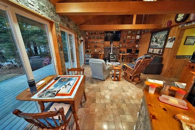 interior space featuring lofted ceiling with beams, wood ceiling, a wood stove, wood walls, and stone finish flooring