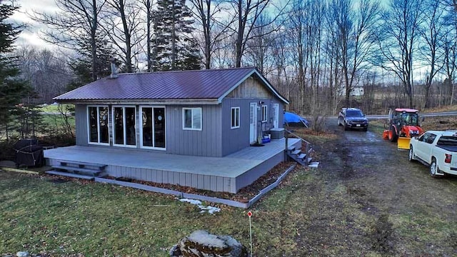 exterior space featuring metal roof, an outdoor structure, driveway, a lawn, and a wooden deck