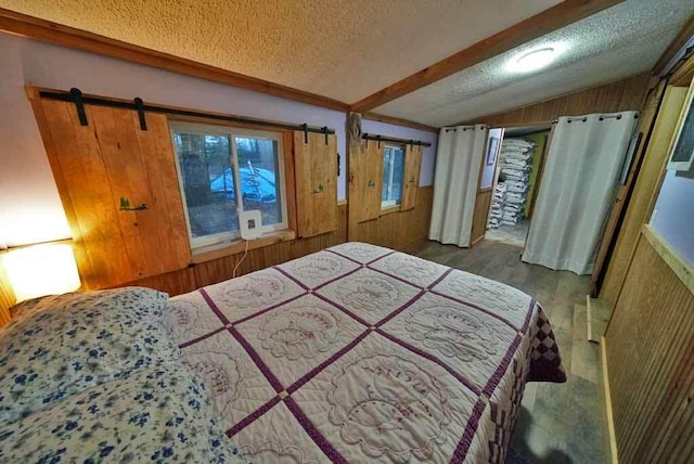 bedroom with a barn door, wooden walls, vaulted ceiling, and a textured ceiling