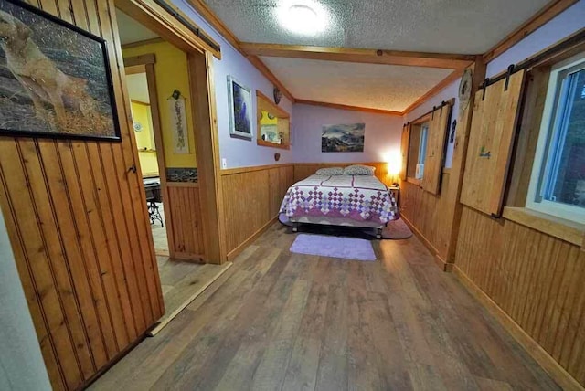 bedroom with a wainscoted wall, a barn door, wooden walls, a textured ceiling, and wood finished floors