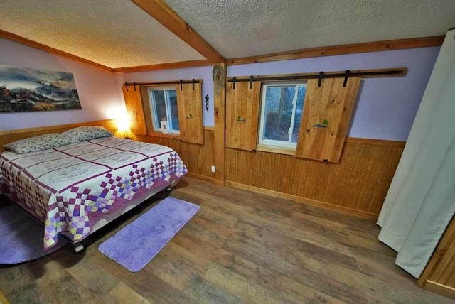 bedroom featuring a textured ceiling, a barn door, wainscoting, and wood finished floors