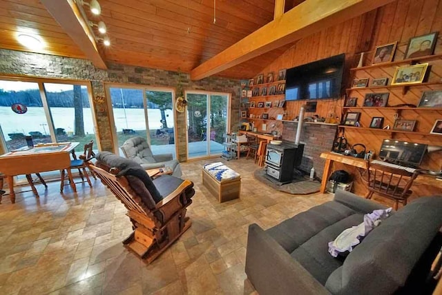 living room featuring wooden walls, lofted ceiling with beams, wooden ceiling, stone finish floor, and a wood stove