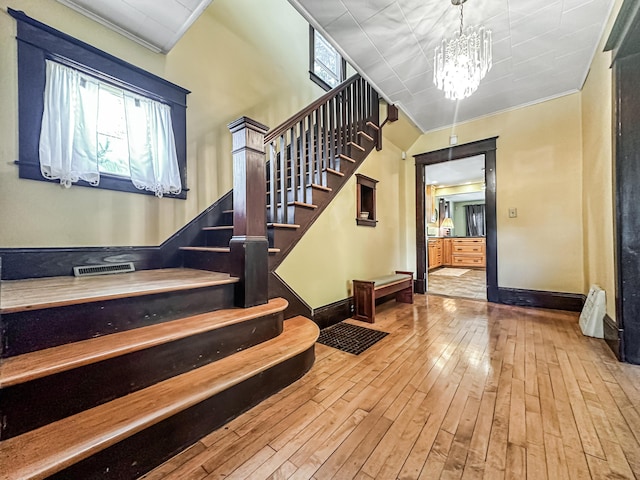 stairway with a wealth of natural light, hardwood / wood-style floors, a notable chandelier, and ornamental molding