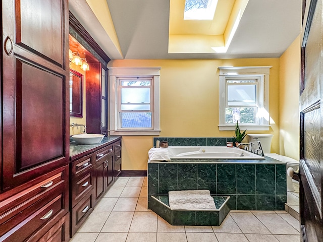 bathroom with vanity, a skylight, tile patterned flooring, a tray ceiling, and tiled bath