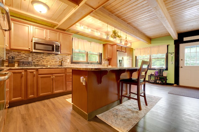 kitchen featuring a kitchen bar, a center island, light hardwood / wood-style floors, stainless steel appliances, and beam ceiling