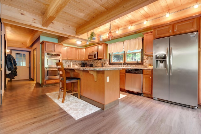 kitchen featuring appliances with stainless steel finishes, a kitchen island, a kitchen bar, beamed ceiling, and light wood-type flooring