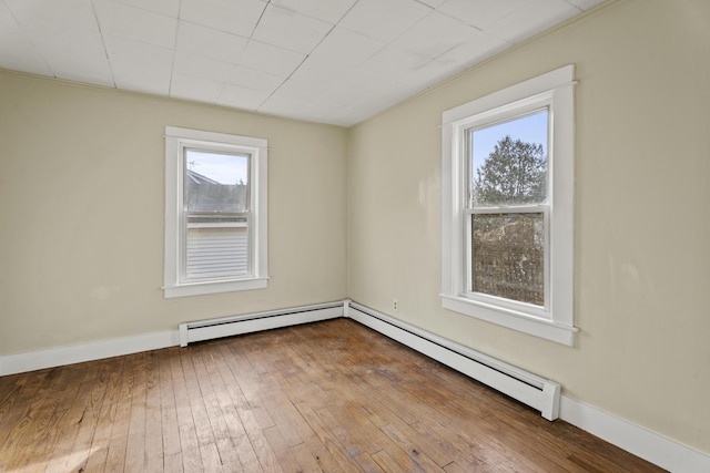 empty room featuring a healthy amount of sunlight, a baseboard heating unit, and hardwood / wood-style flooring