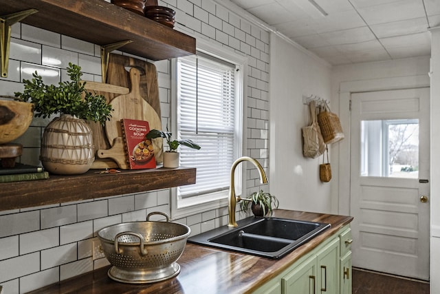 kitchen featuring butcher block counters, sink, green cabinets, decorative backsplash, and ornamental molding