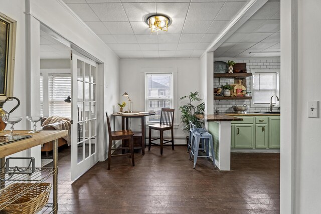 bar with sink, dark wood-type flooring, a baseboard radiator, green cabinets, and backsplash