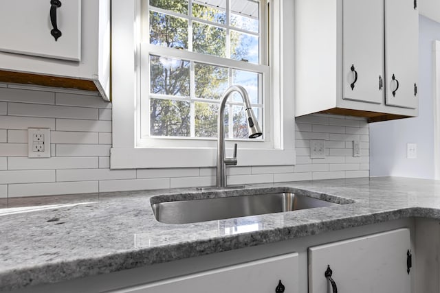 room details featuring light stone counters, tasteful backsplash, white cabinetry, and sink