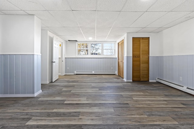 spare room featuring a paneled ceiling, dark wood-type flooring, and a baseboard heating unit