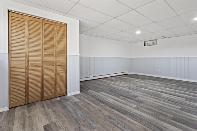 unfurnished bedroom featuring hardwood / wood-style floors, a drop ceiling, a baseboard radiator, and a closet