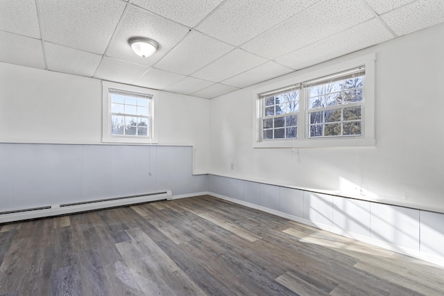 empty room featuring dark hardwood / wood-style flooring, a baseboard radiator, and a drop ceiling