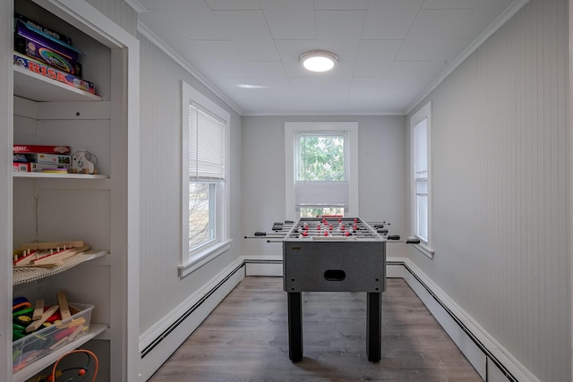 recreation room with baseboard heating, wood-type flooring, and ornamental molding