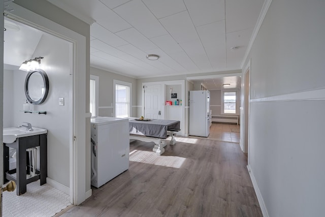 corridor with crown molding, sink, light wood-type flooring, radiator heating unit, and washer / clothes dryer