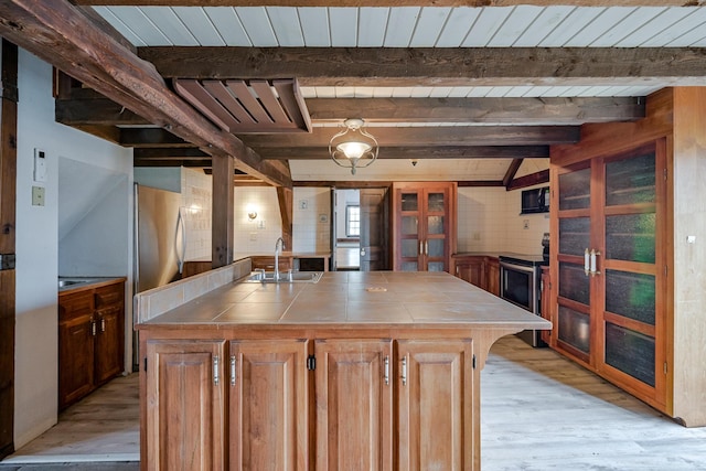 kitchen with beamed ceiling, appliances with stainless steel finishes, a center island, and sink