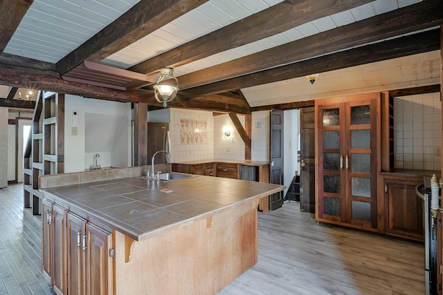 kitchen featuring sink, beamed ceiling, light hardwood / wood-style floors, a breakfast bar, and a kitchen island