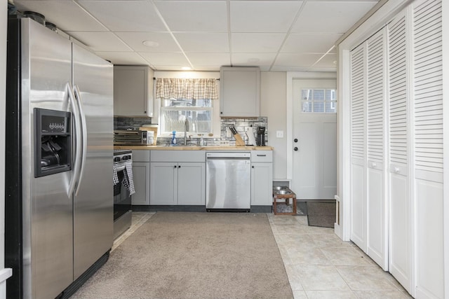 kitchen featuring a paneled ceiling, decorative backsplash, gray cabinets, and stainless steel appliances