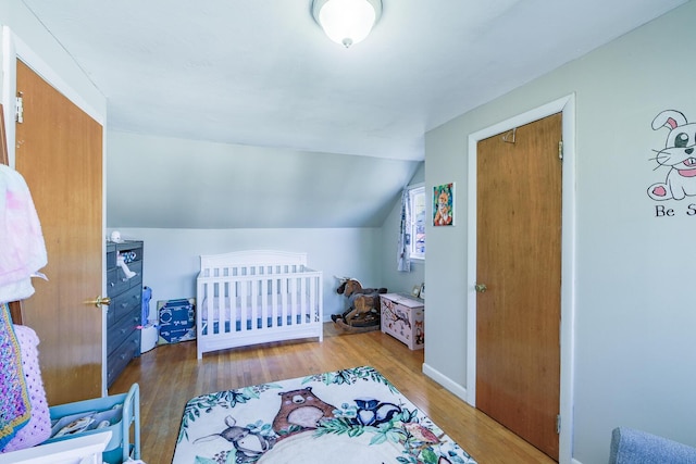 bedroom with hardwood / wood-style flooring, vaulted ceiling, and a nursery area