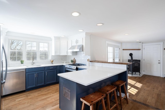 kitchen featuring appliances with stainless steel finishes, blue cabinets, white cabinetry, sink, and kitchen peninsula