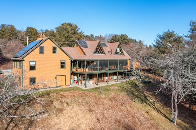 rear view of property with a sunroom, a yard, a patio, and solar panels