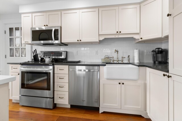 kitchen with sink, backsplash, wood-type flooring, white cabinets, and appliances with stainless steel finishes