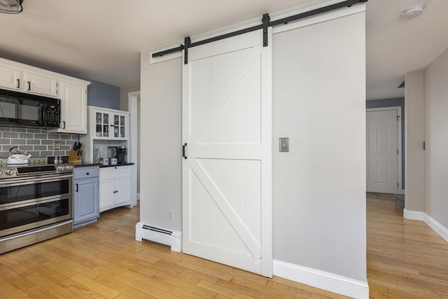 kitchen with backsplash, a baseboard heating unit, stainless steel stove, a barn door, and white cabinetry