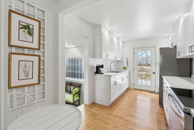 kitchen with white cabinets, light wood-type flooring, range with electric stovetop, and sink