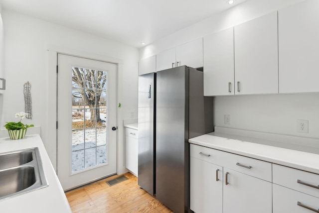 kitchen featuring white cabinets, stainless steel fridge, light hardwood / wood-style flooring, and sink