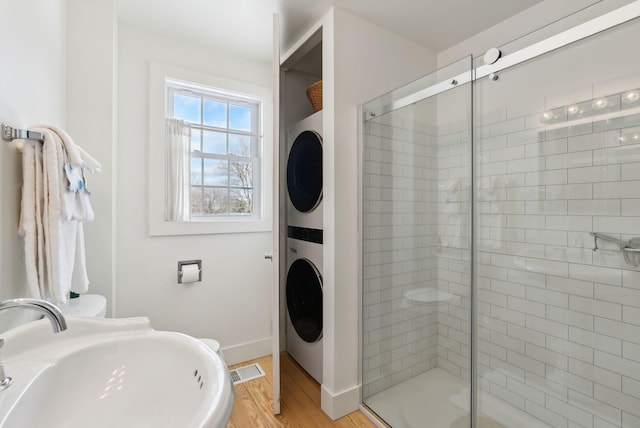 bathroom with sink, walk in shower, stacked washing maching and dryer, and hardwood / wood-style flooring