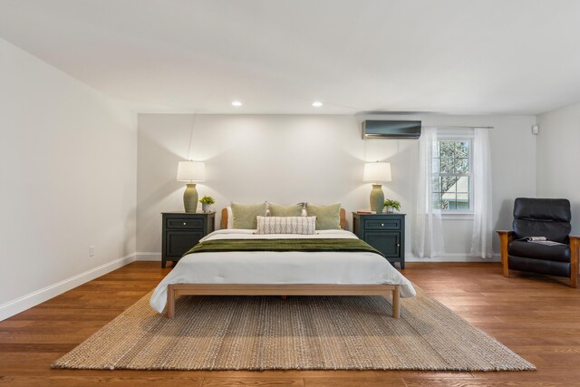bedroom with an AC wall unit, recessed lighting, baseboards, and wood finished floors