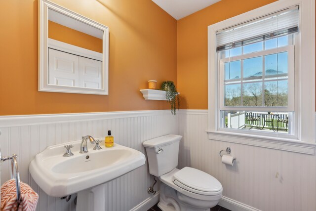 half bathroom featuring toilet, a sink, and a wainscoted wall
