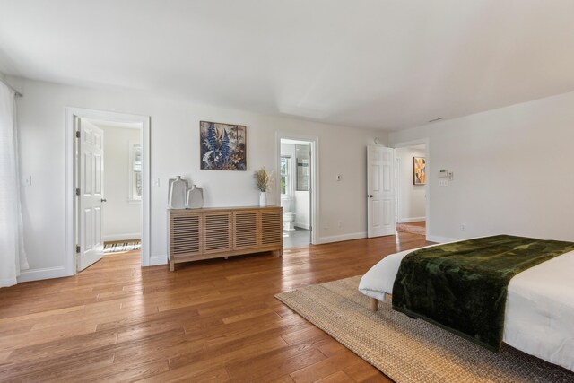 bedroom with baseboards, ensuite bathroom, and light wood-style flooring