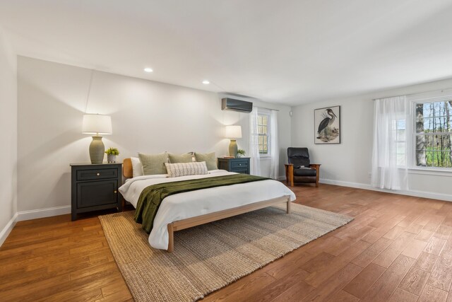 bedroom featuring baseboards, a wall unit AC, recessed lighting, and wood finished floors
