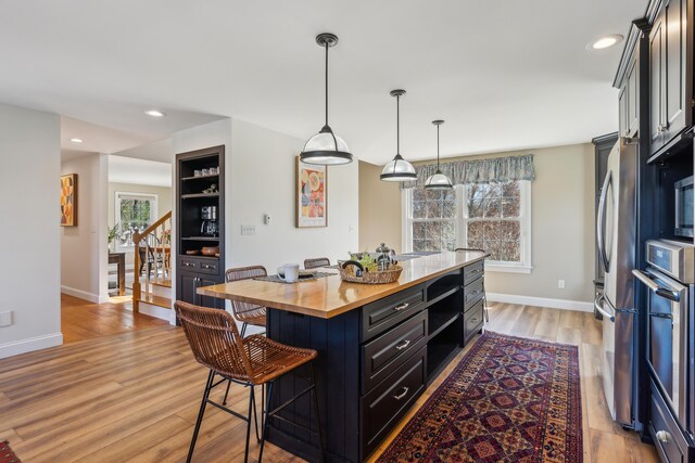 kitchen featuring a breakfast bar area, wooden counters, baseboards, light wood finished floors, and stainless steel appliances