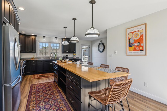 kitchen with wood finished floors, butcher block countertops, a breakfast bar area, a sink, and appliances with stainless steel finishes