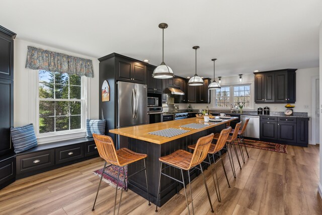 kitchen featuring light wood-type flooring, appliances with stainless steel finishes, wooden counters, and a kitchen breakfast bar