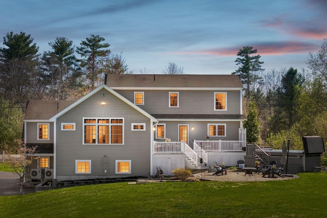 back of property with a lawn, a wooden deck, a shingled roof, stairway, and a fire pit