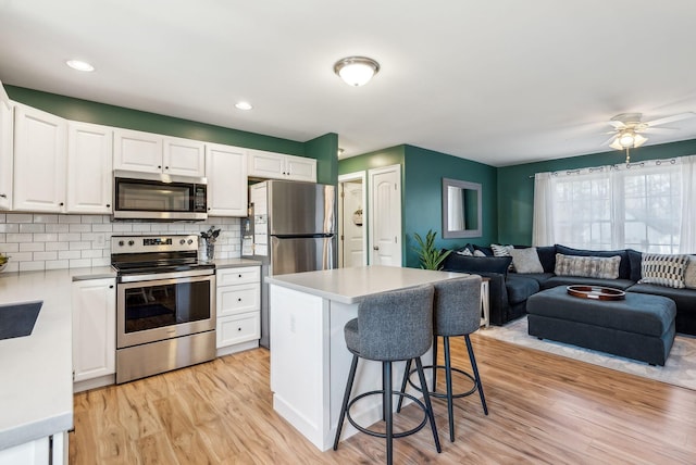 kitchen with stainless steel appliances, white cabinetry, a center island, light hardwood / wood-style floors, and decorative backsplash