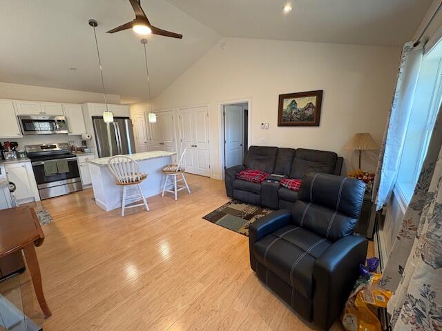 living room with light hardwood / wood-style floors, high vaulted ceiling, and ceiling fan