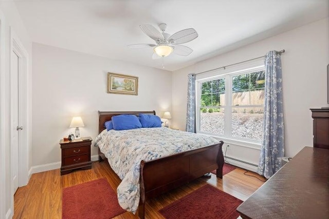 bedroom with ceiling fan, wood-type flooring, and a baseboard heating unit