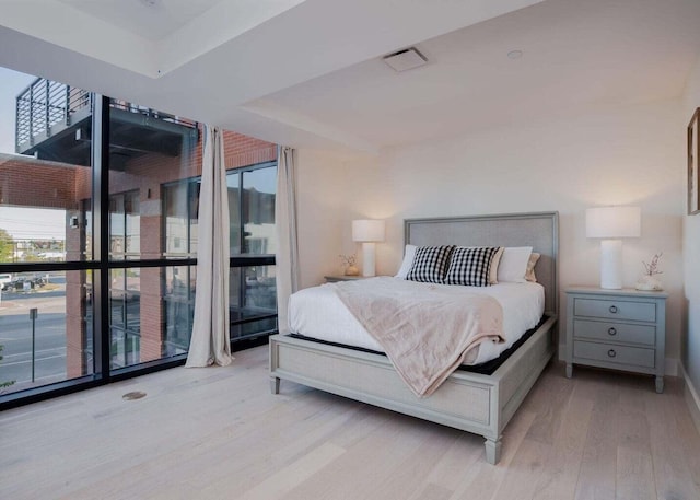 bedroom featuring a raised ceiling, a wall of windows, light wood-type flooring, and multiple windows