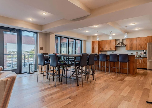 bar with stainless steel refrigerator, wall chimney exhaust hood, hanging light fixtures, and light hardwood / wood-style floors