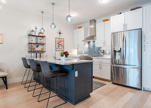 kitchen with light stone countertops, stainless steel refrigerator with ice dispenser, wall chimney exhaust hood, pendant lighting, and white cabinetry