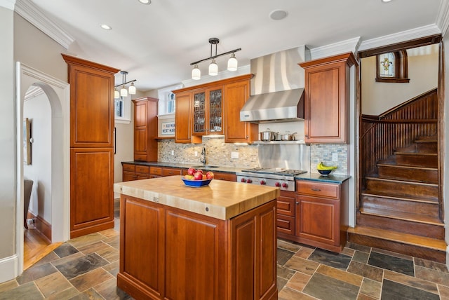 kitchen featuring a kitchen island, decorative light fixtures, wall chimney range hood, butcher block countertops, and stainless steel gas stovetop